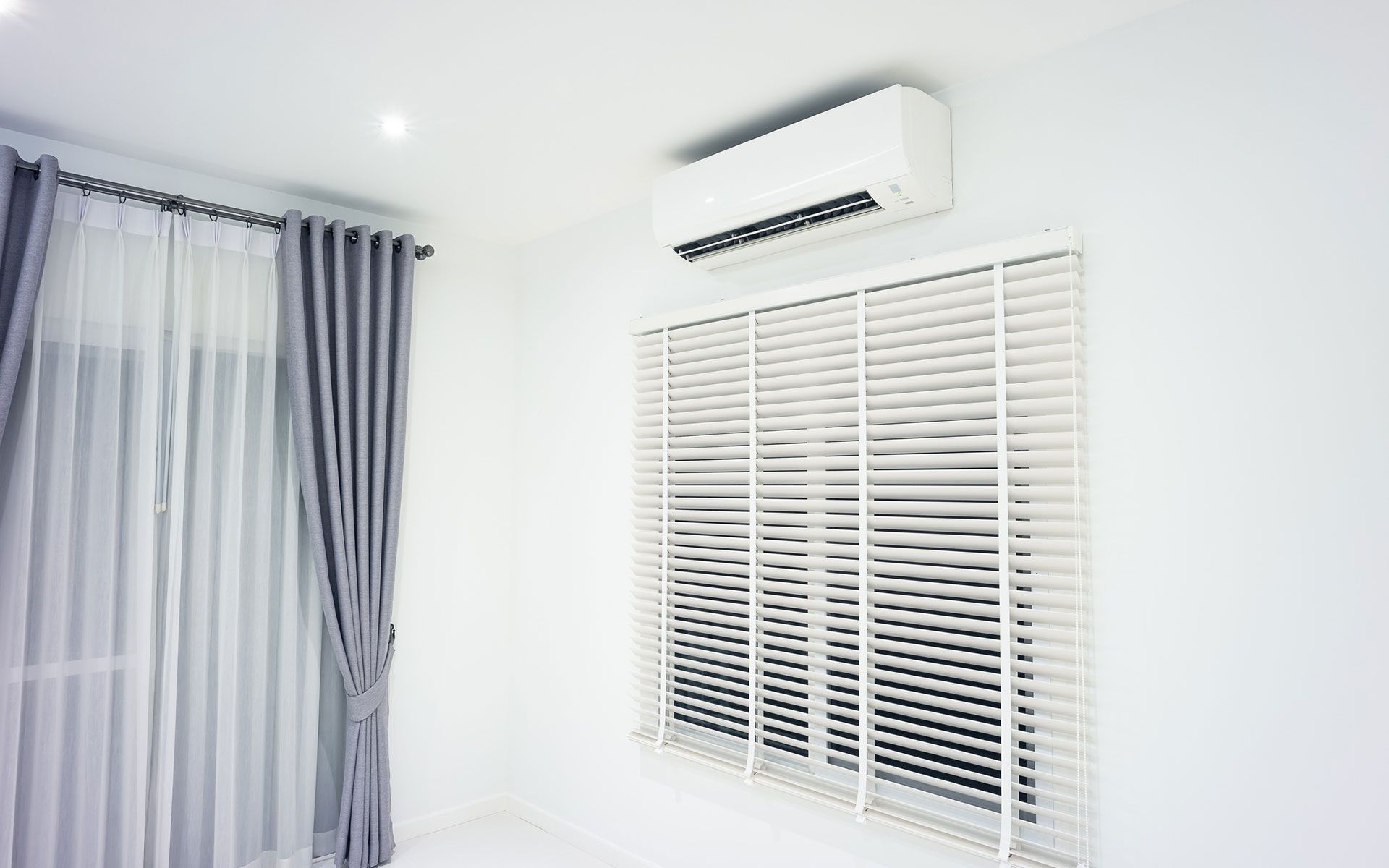 There is a window with blinds and a air conditioner on the wall.