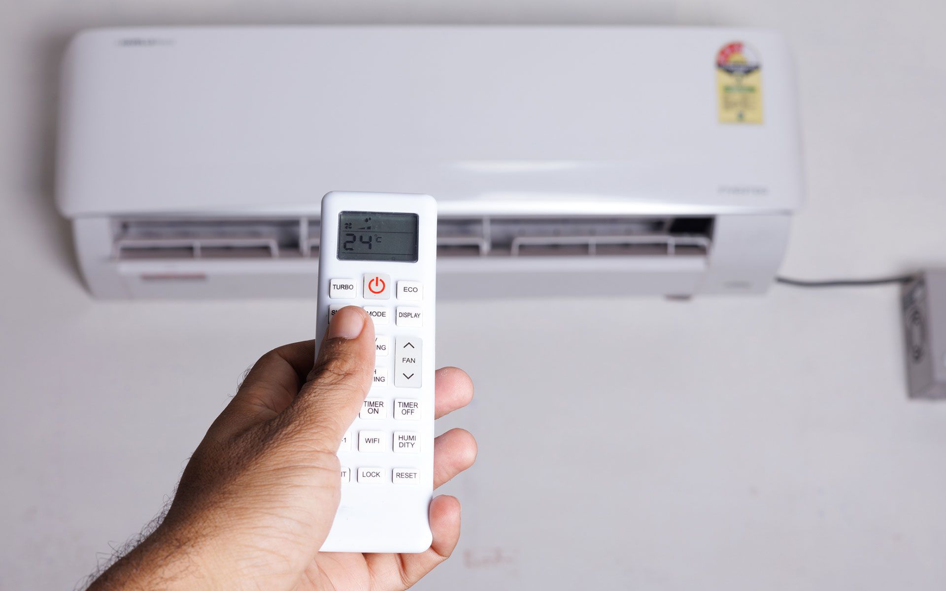 A person is holding a remote control in front of an air conditioner.