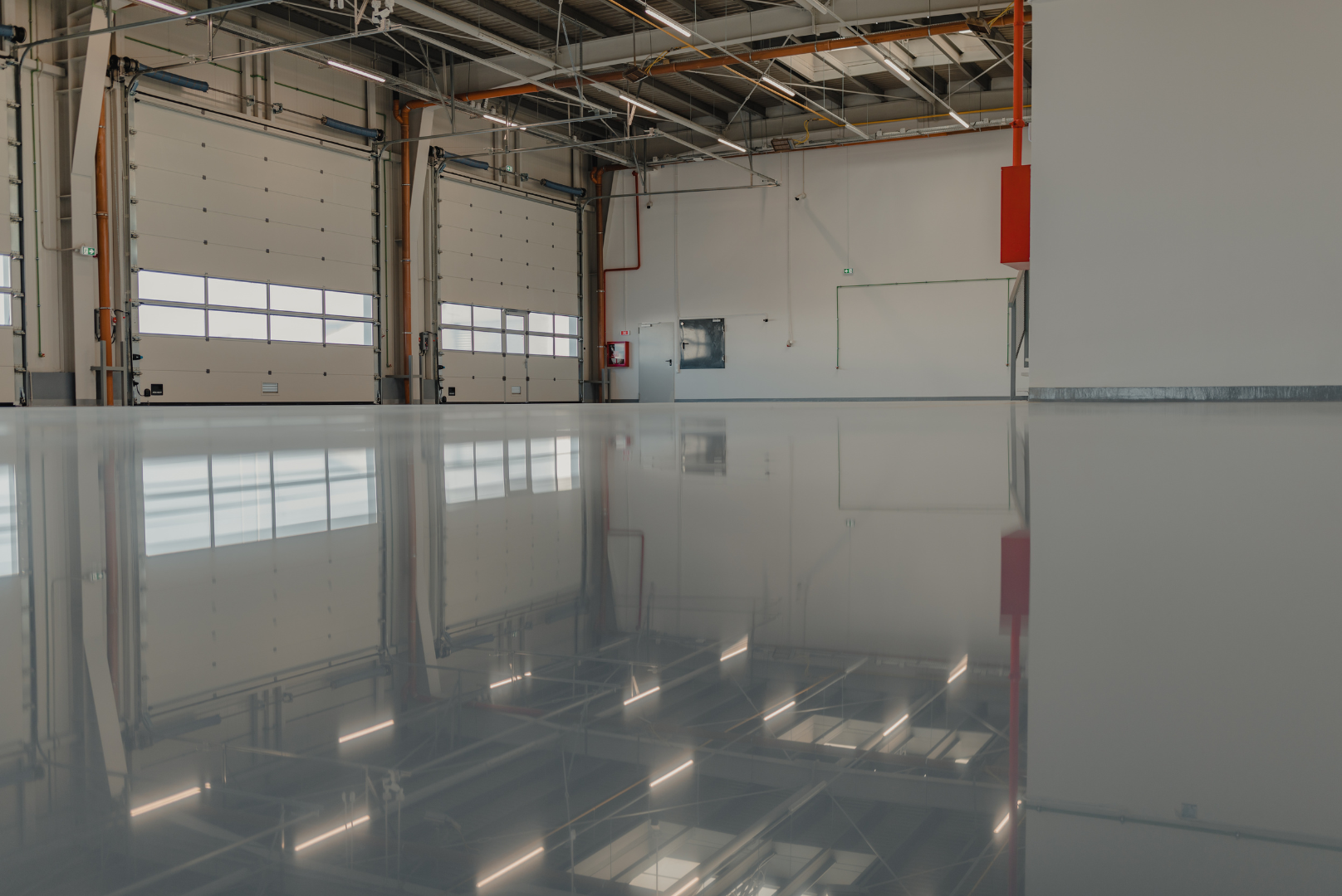 Glossy gray floor reflects a warehouse interior, showing doors, windows, and overhead lighting.