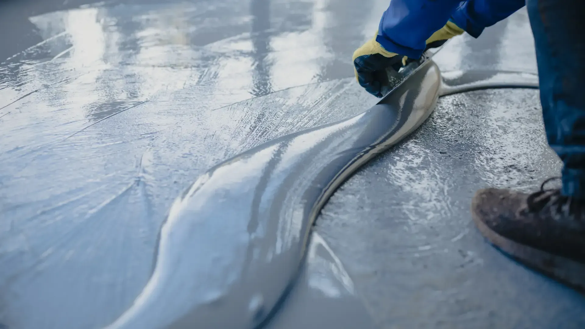 Person using a tool to spread gray sealant on a concrete surface.