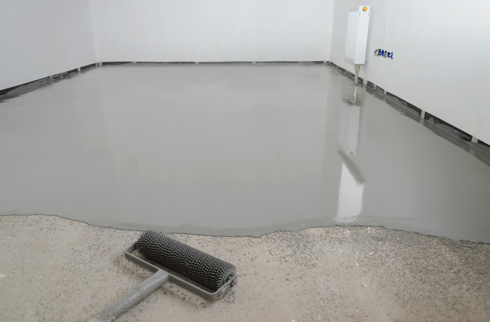 Garage floor being coated with gray epoxy, roller in foreground.