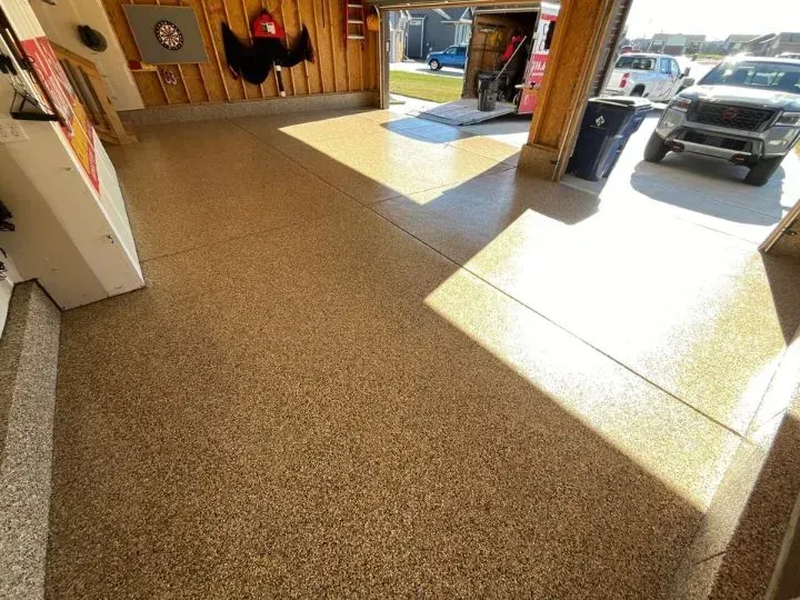 Garage interior with a tan speckled epoxy floor. Garage door open to a driveway with a truck.