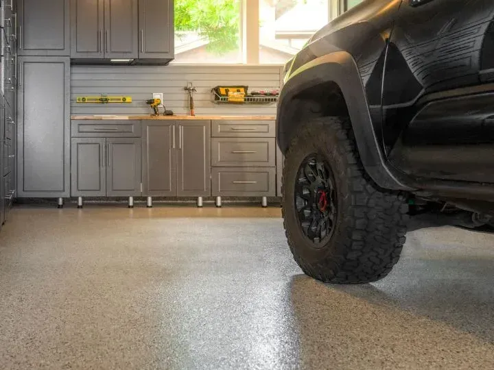 Black truck parked in a garage with gray cabinets, a wooden countertop, and speckled flooring.