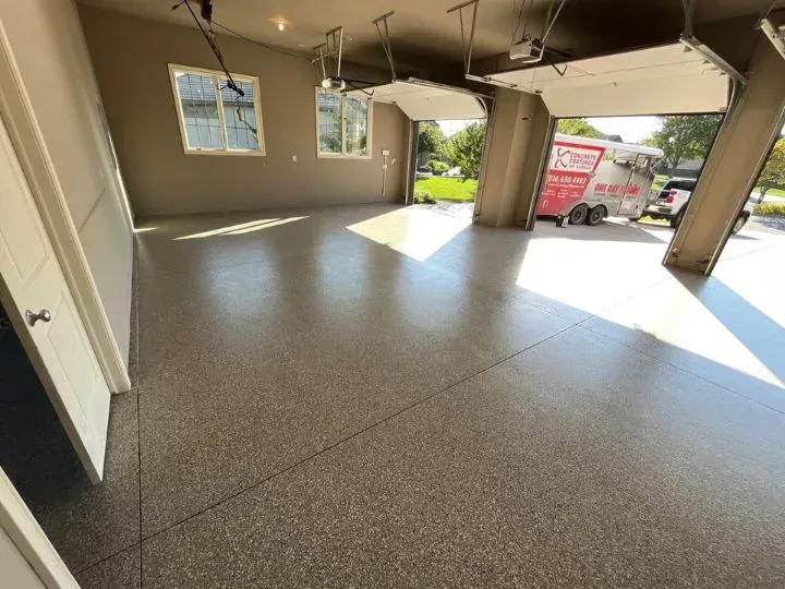 Garage with epoxy floor, open door reveals parked trailer on sunny day.