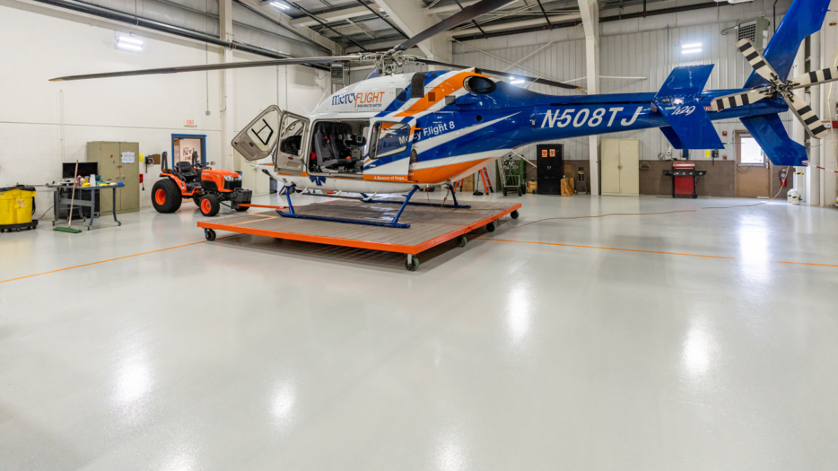 Empty, spacious industrial warehouse with a shiny, grey epoxy floor and large overhead doors.