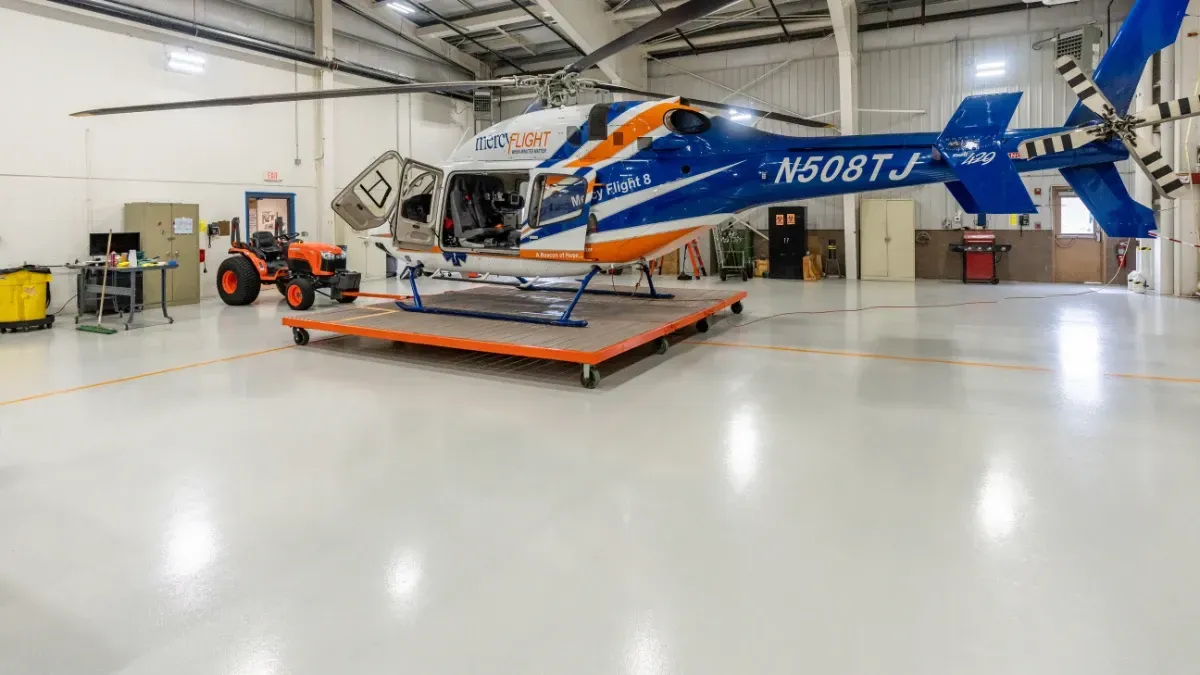 Empty, spacious industrial warehouse with a shiny, grey epoxy floor and large overhead doors.