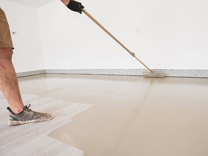 Person applying epoxy floor coating with a roller in a garage.