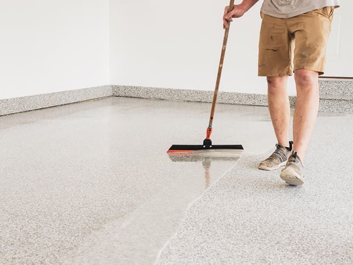 Person applies epoxy to a garage floor with a squeegee.