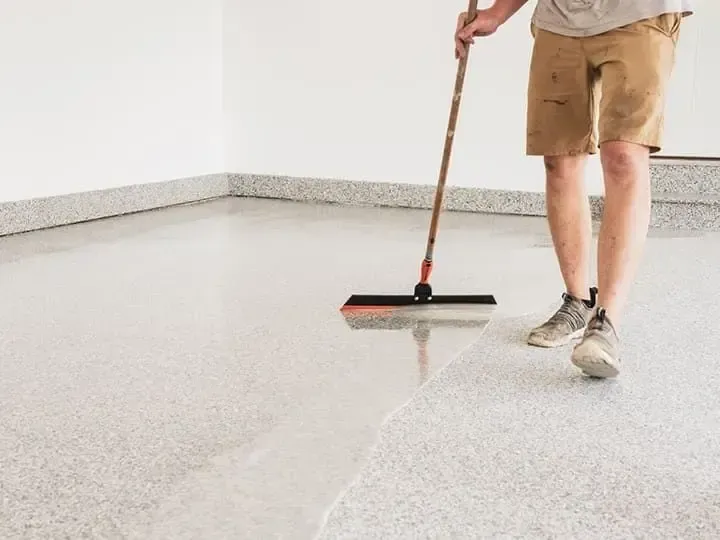 Person applies epoxy to a garage floor with a squeegee.