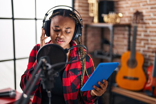 Woman in headphones singing into microphone, holding tablet in recording studio.