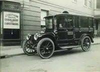 A black and white photo of an old car parked on the side of the road.