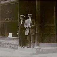 Two men in suits and hats are standing in front of a building.