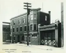 A black and white photo of a brick building with a fire station in front of it.