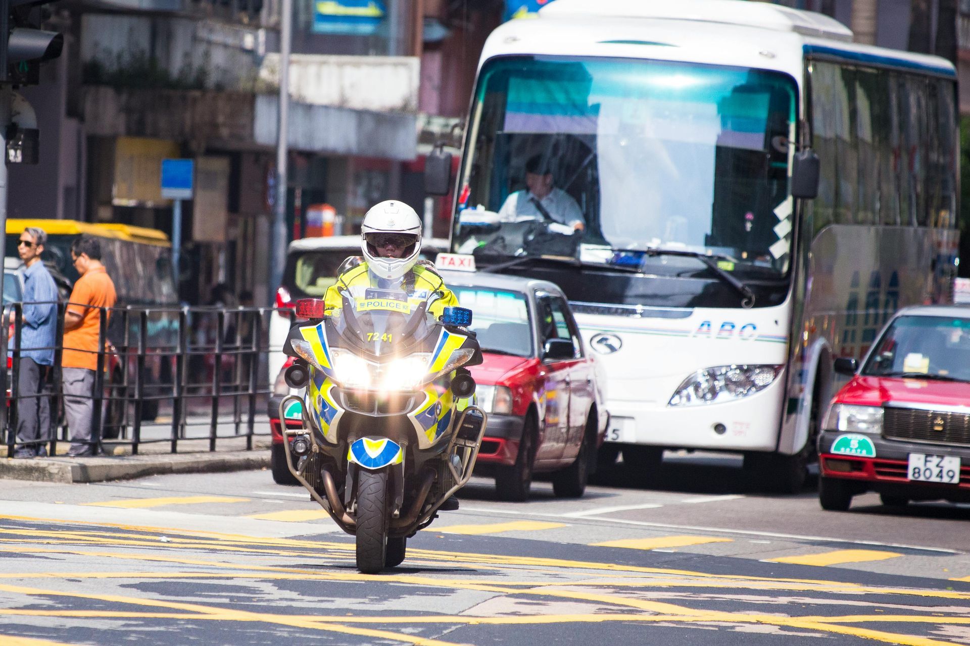 Policía en motocicleta en medio del tráfico, Hong Kong. Cerca hay un autobús y taxis rojos.