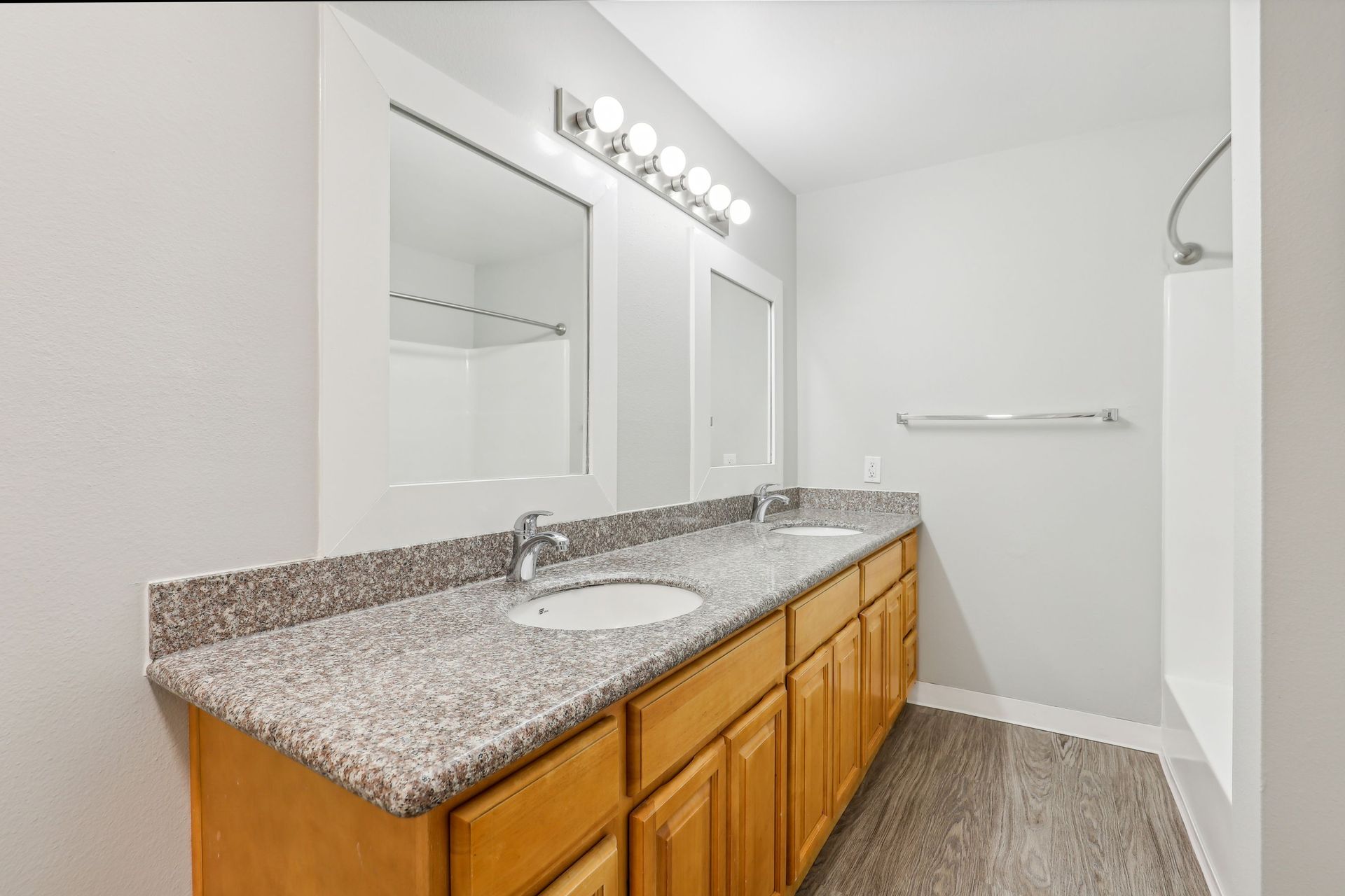 Two-sink bathroom vanity with granite countertop, large mirror, and bright row of lights.