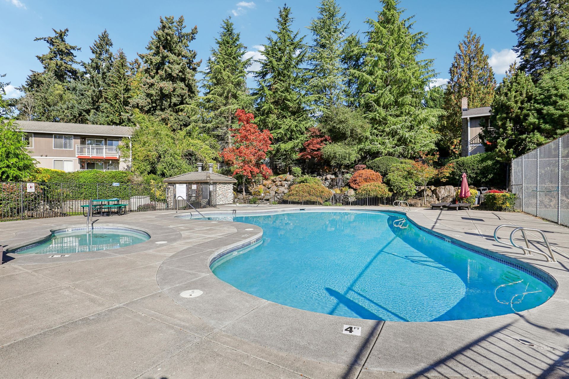 Outdoor apartment pool with surrounding lounge area, trees, and clear blue water.