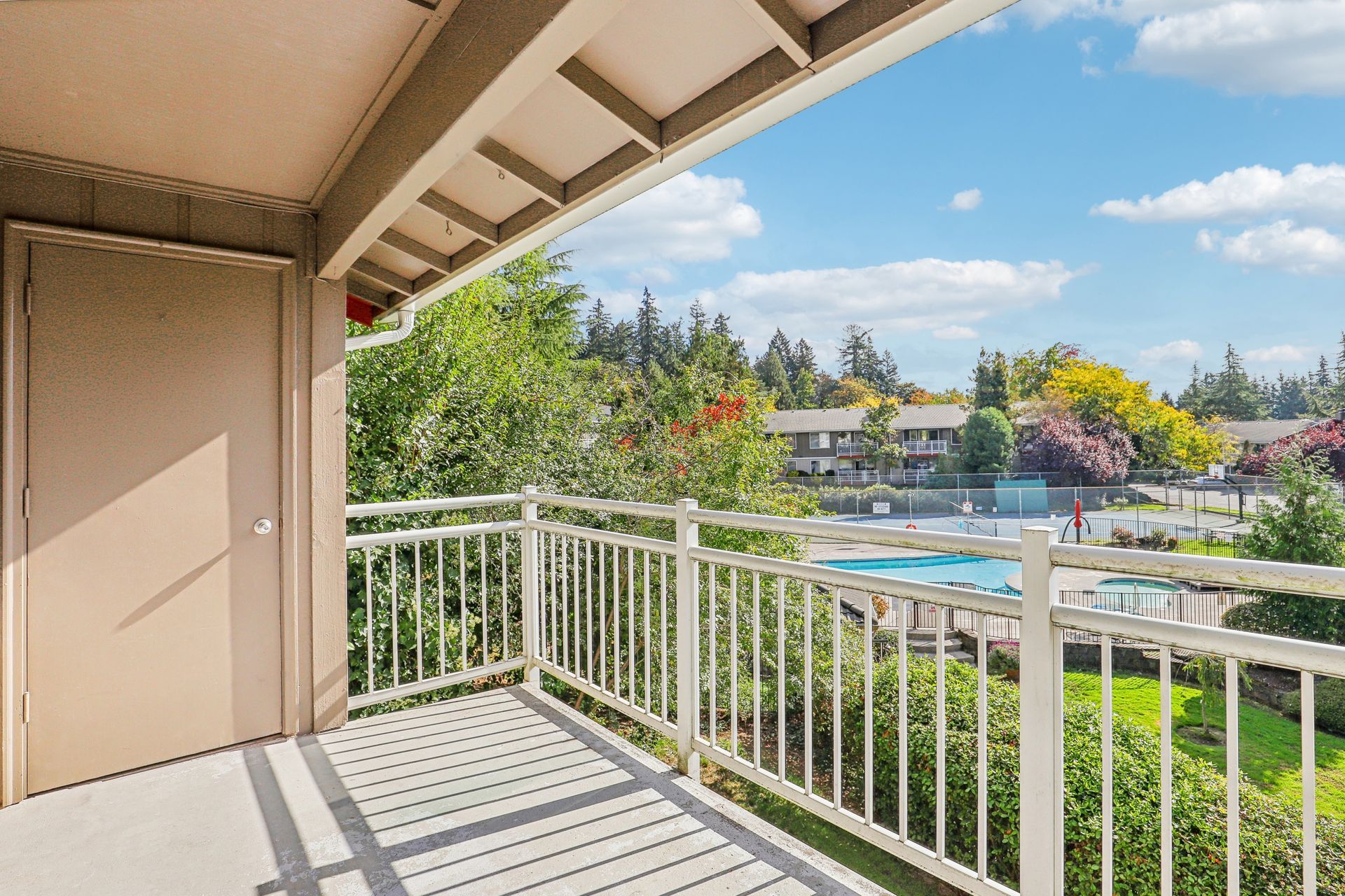Balcony view overlooking a community pool and tennis court with trees.
