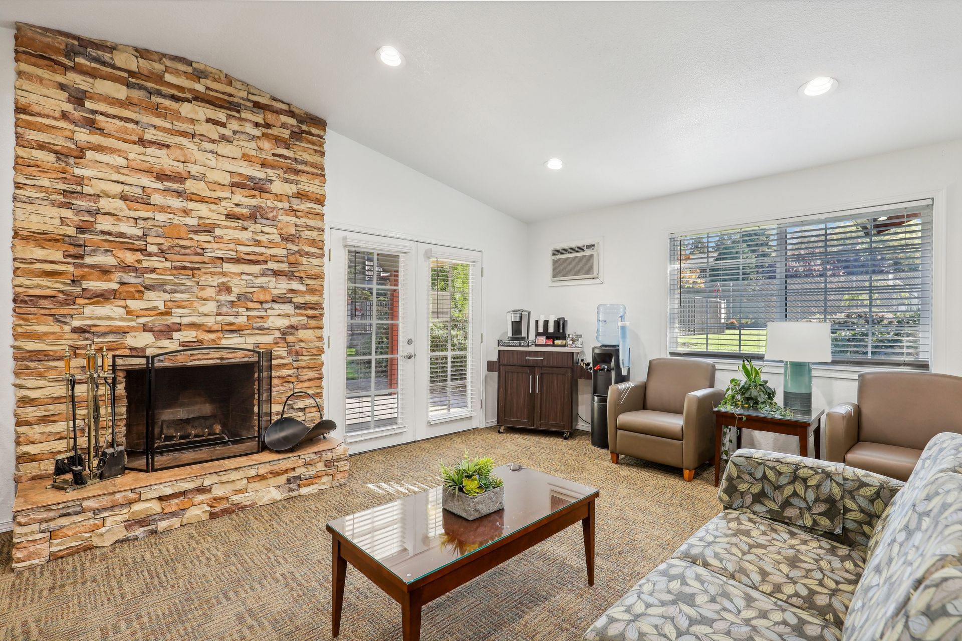 Living room with a stacked stone fireplace, beige seating, and large windows.