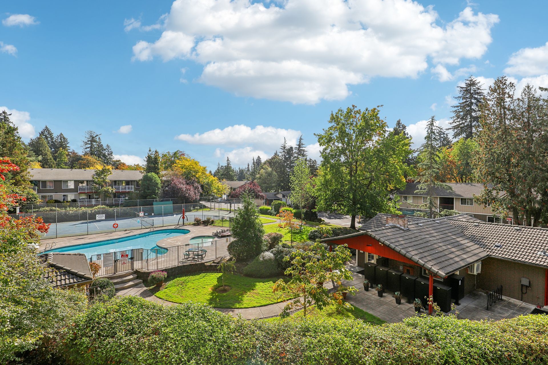 Outdoor pool area with landscaping, tennis court, and clubhouse at apartment complex.