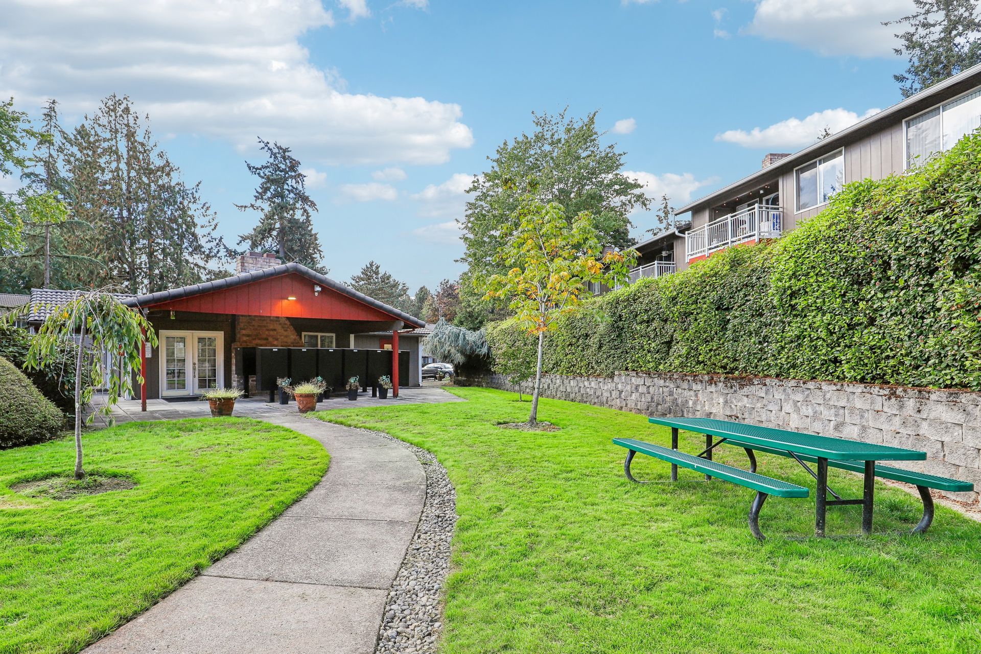 Outdoor community courtyard with curved walkway, lawn, and a red-roofed clubhouse.