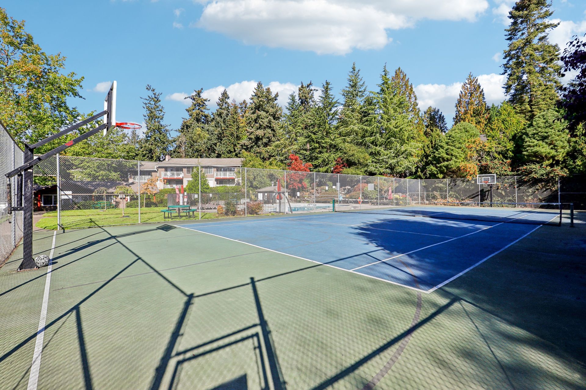 Outdoor fenced basketball court at an apartment community with trees and buildings in the background.