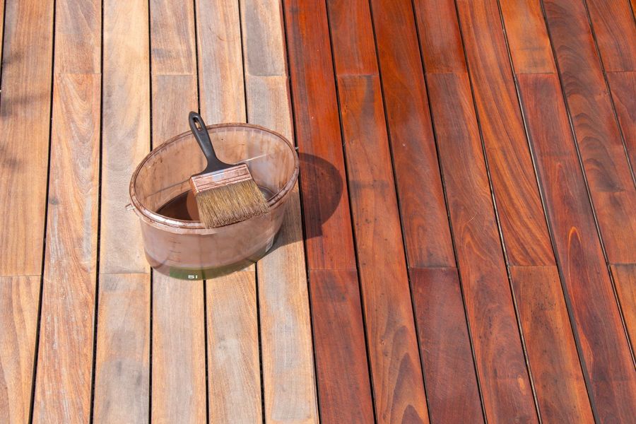 A wooden deck is being painted with a brush and a bowl of paint.