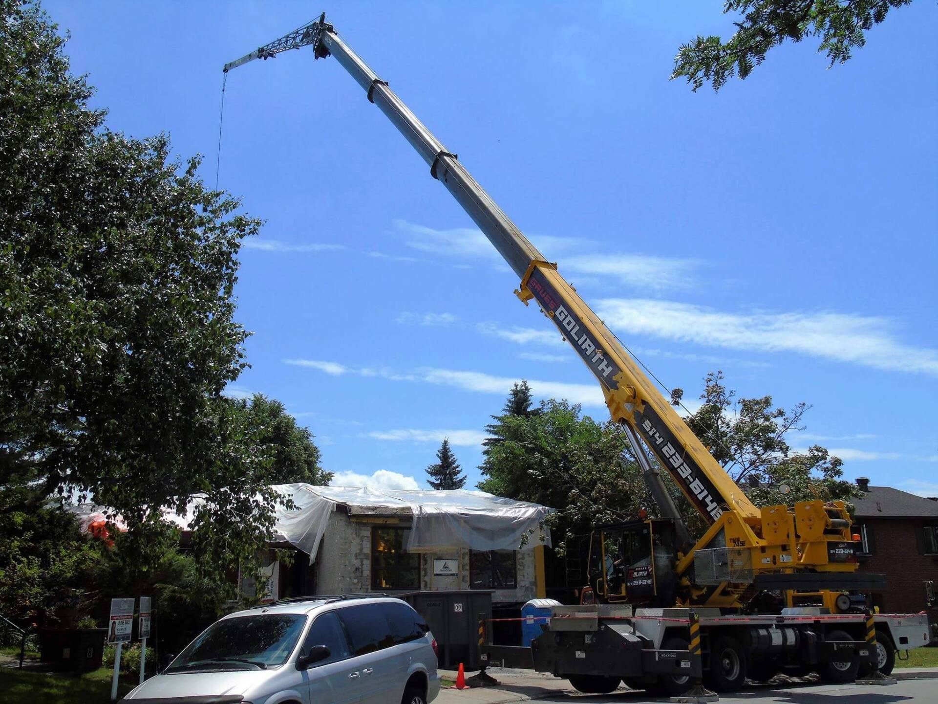 Une grue jaune soulève une maison en construction par une journée ensoleillée.