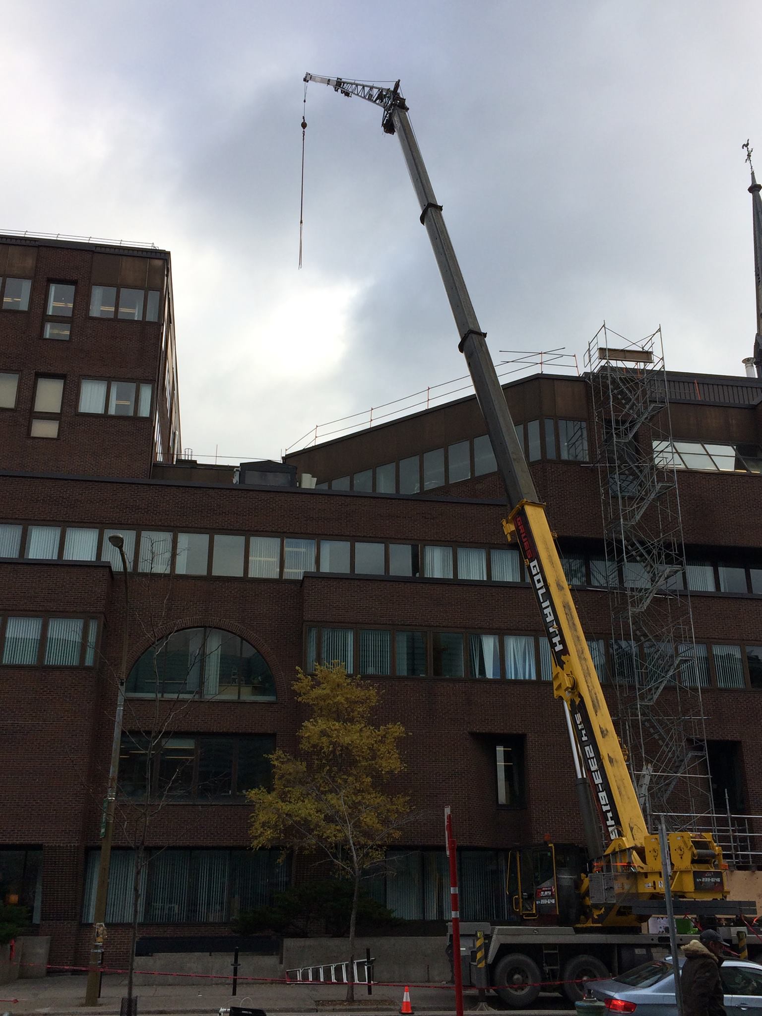 La grue s'étend bien au-dessus d'un bâtiment en briques, avec un fond de ciel nuageux.