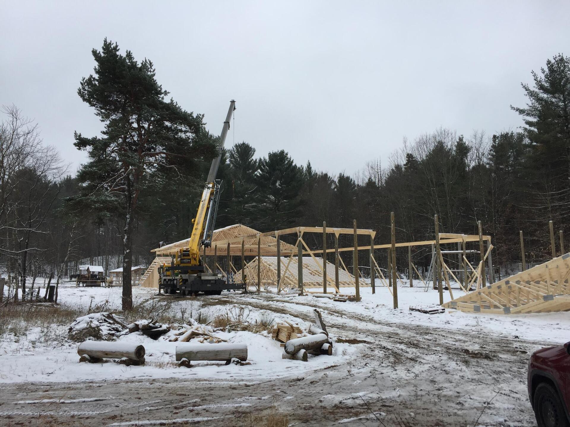 Construction d'un bâtiment en bois avec une grue un jour de neige dans une zone boisée.