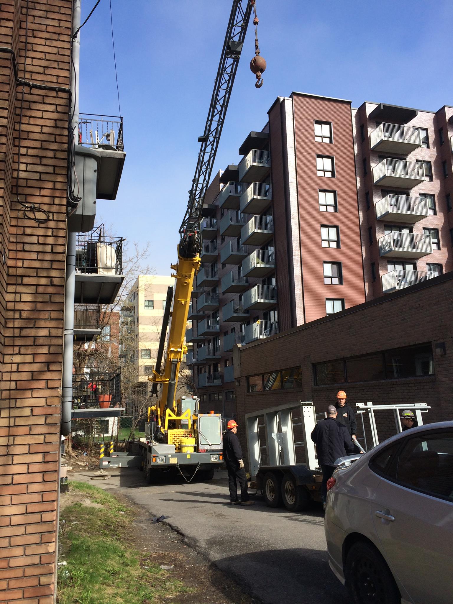 Grue jaune à côté d'un grand immeuble d'appartements marron, ouvriers du bâtiment près d'un camion.
