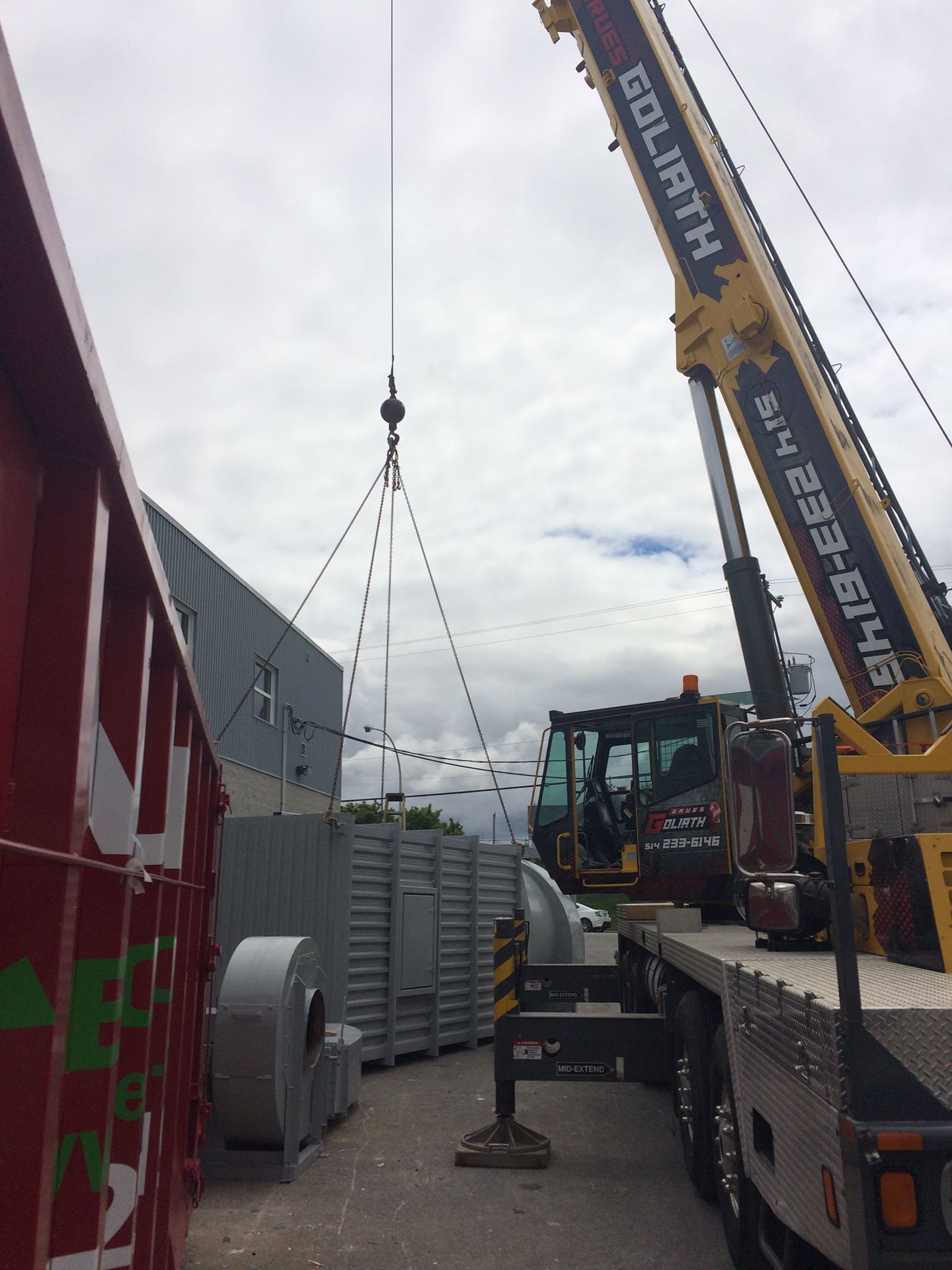 Une grue soulevant un équipement CVC près d'un bâtiment par une journée ensoleillée.