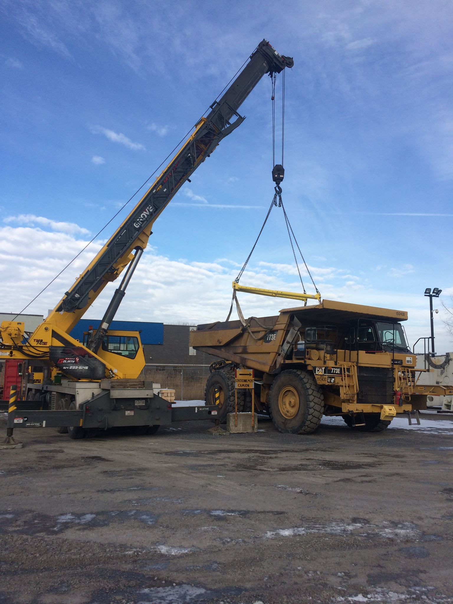 Une grue jaune soulevant un gros camion minier jaune sous un ciel bleu.