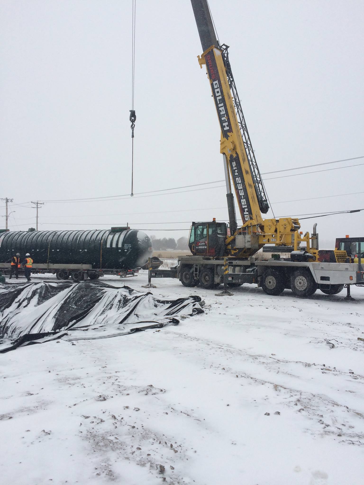 Grue soulevant un grand réservoir vert dans un décor extérieur enneigé.