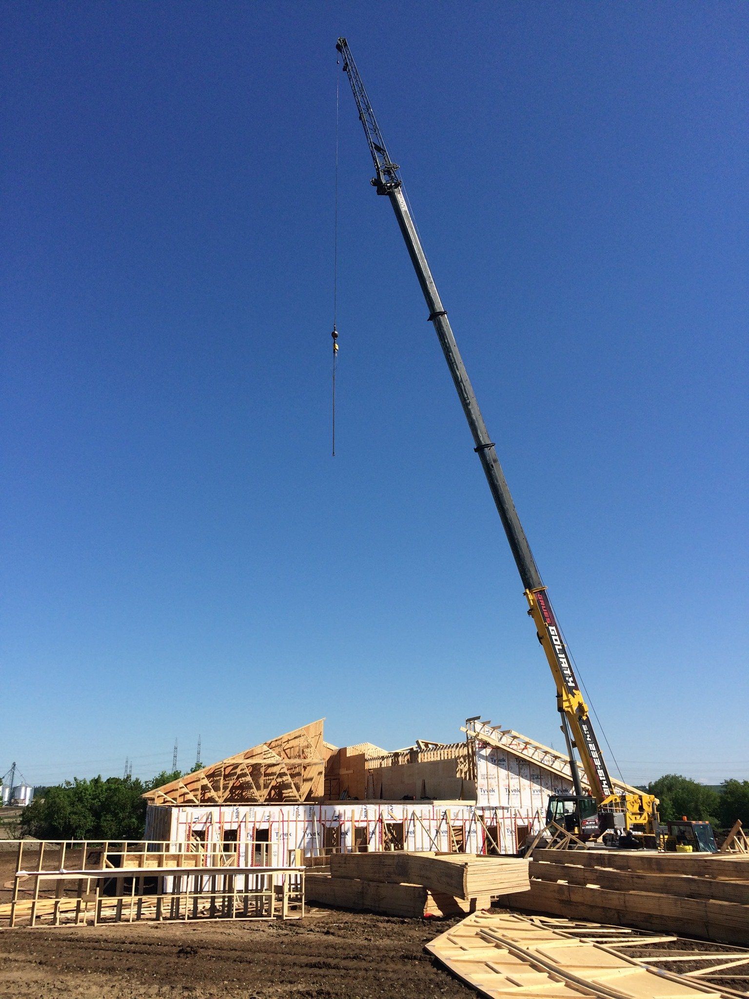 Chantier de construction : une grue soulève un élément de construction sous un ciel bleu. Bois de construction, structure inachevée.