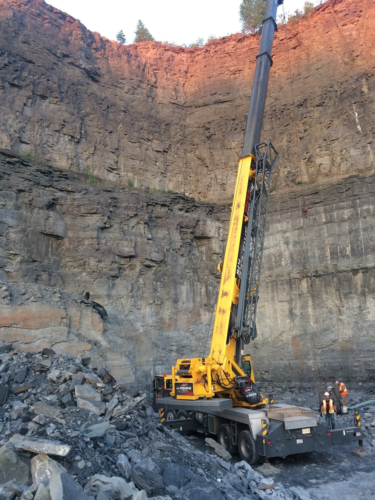 Grue jaune contre un mur rocheux. Ouvriers du bâtiment. Le décor semble être une carrière.