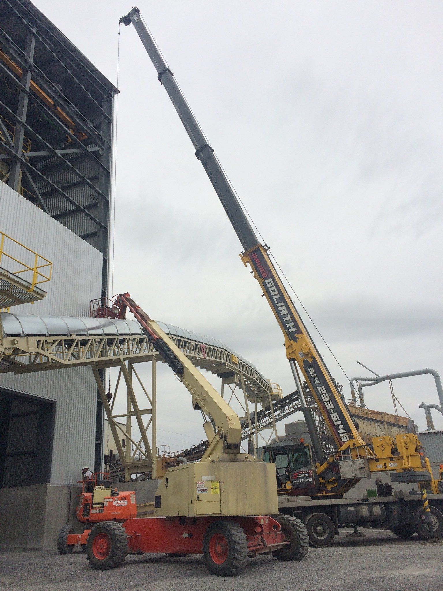 Une grue et une nacelle élévatrice à côté d'un grand bâtiment industriel.