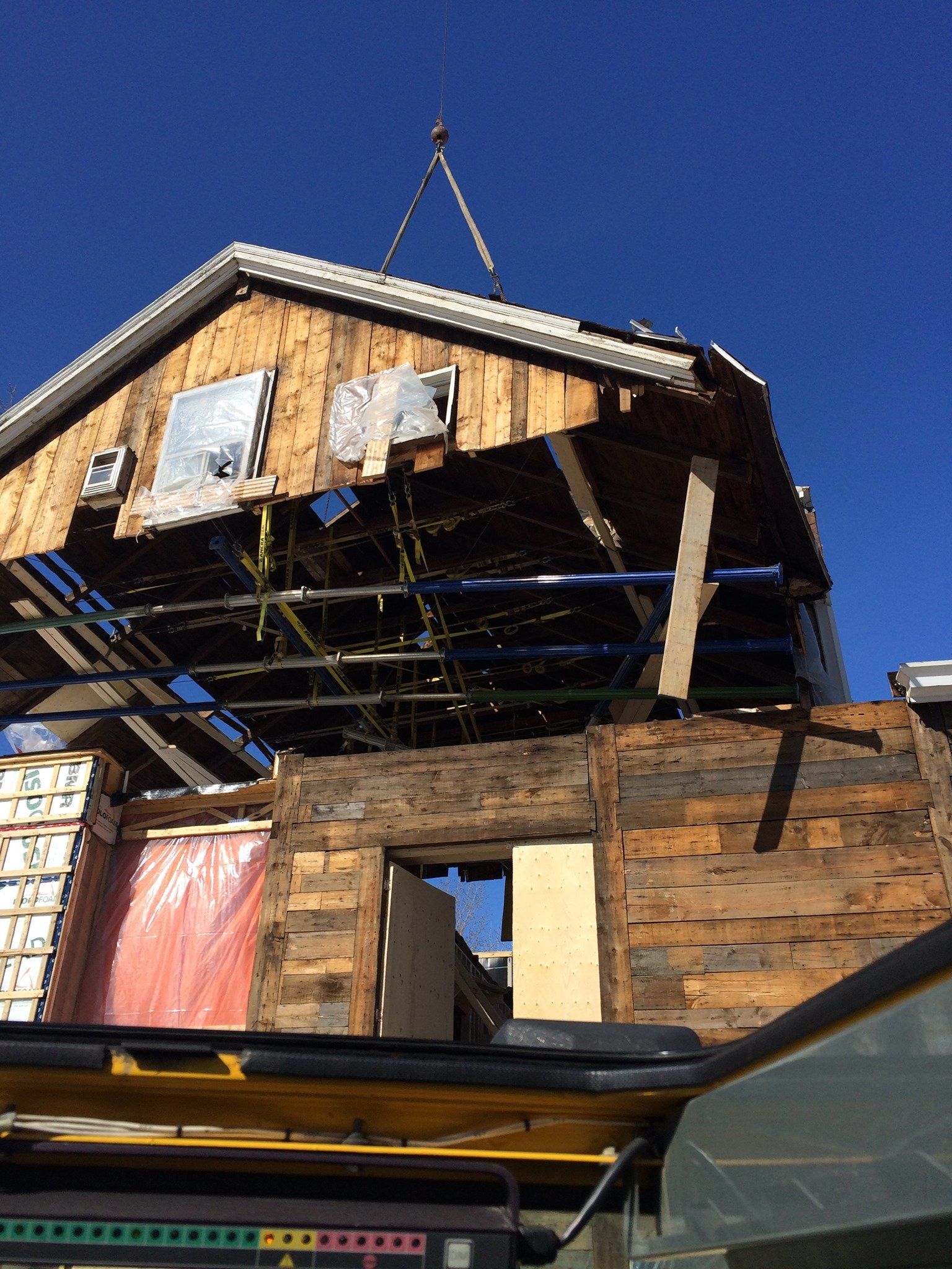 Une grue soulevant le toit d'un bâtiment à ossature de bois contre un ciel bleu clair.