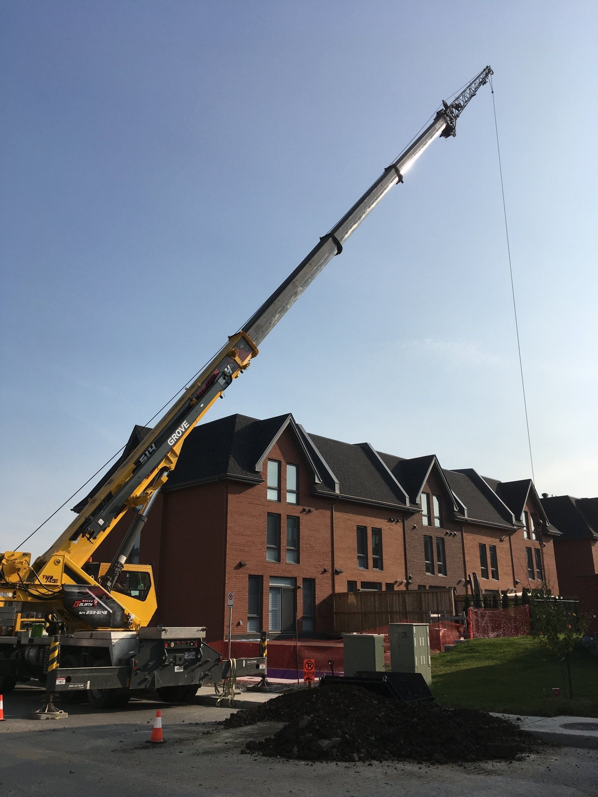 Une grande grue jaune s'étend vers le haut, avec une rangée de maisons en briques en arrière-plan, sous un ciel bleu.