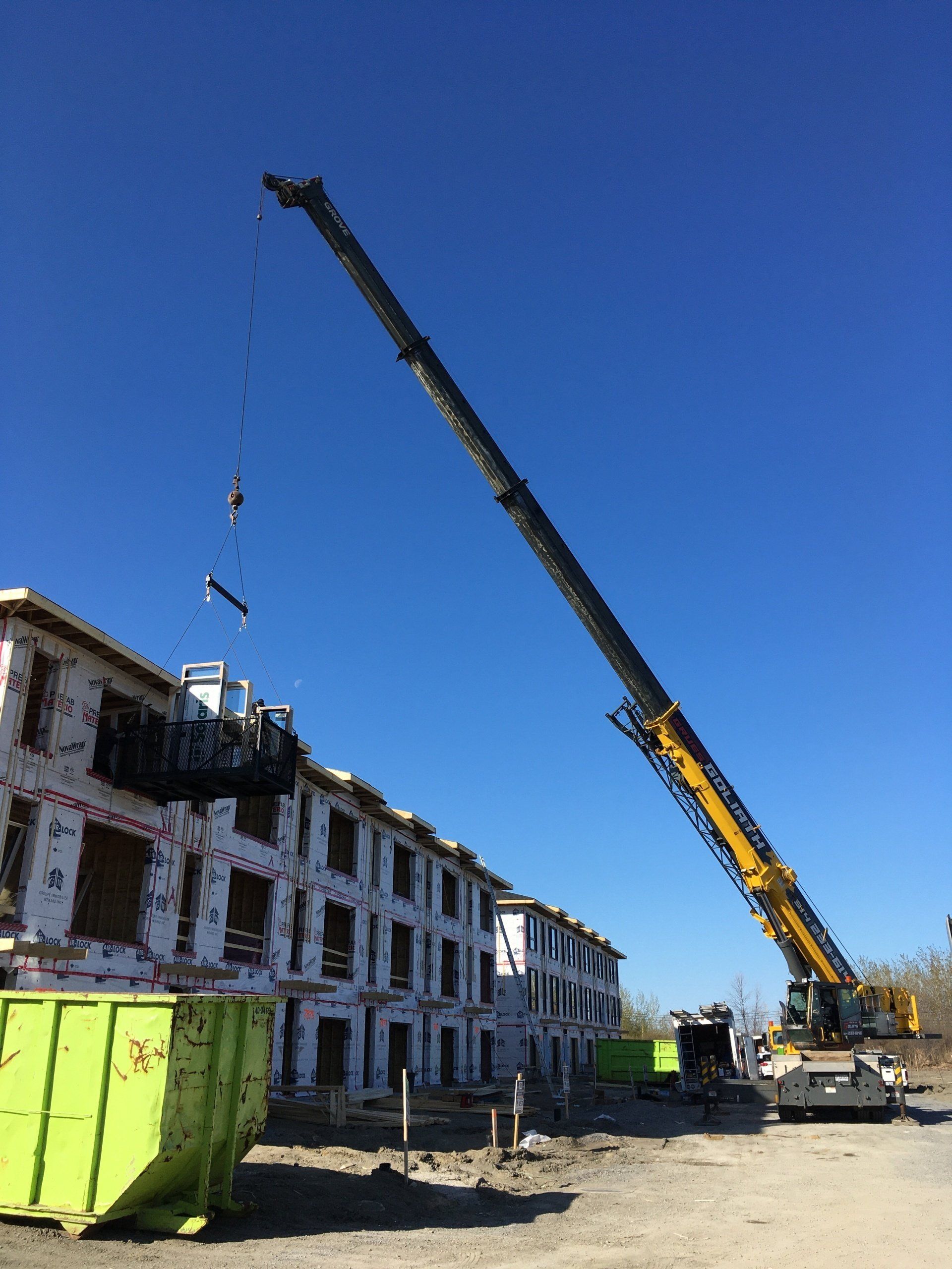 Grue de construction soulevant une poutre métallique sur un chantier de construction à plusieurs étages par une journée claire et ensoleillée.