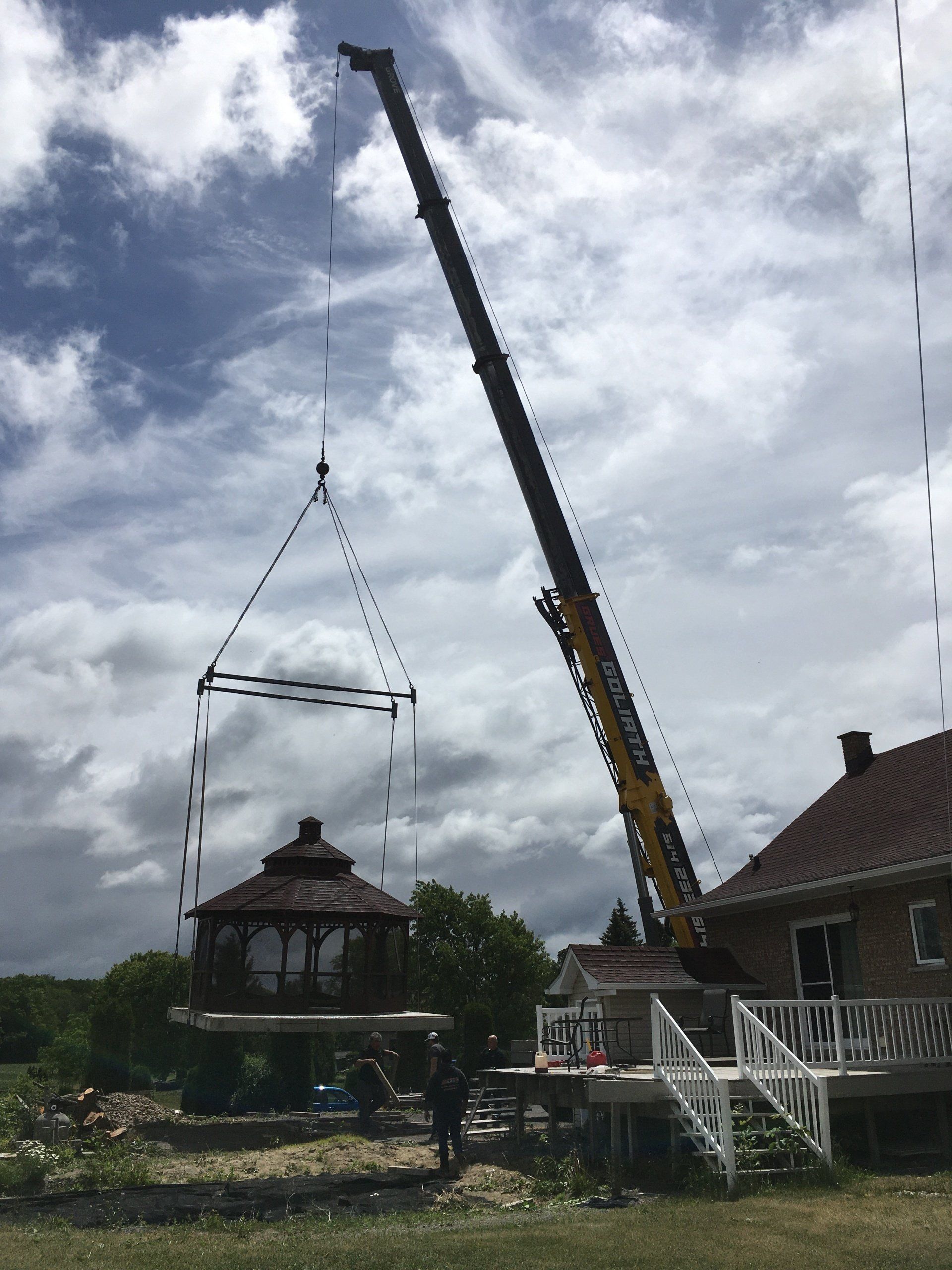 Grue soulevant le toit d'un belvédère près d'une maison par une journée ensoleillée.