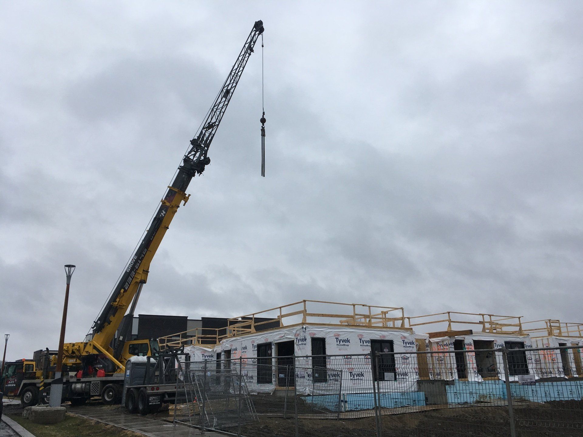 Une grue jaune soulevant quelque chose au-dessus d'un bâtiment en construction par une journée nuageuse.