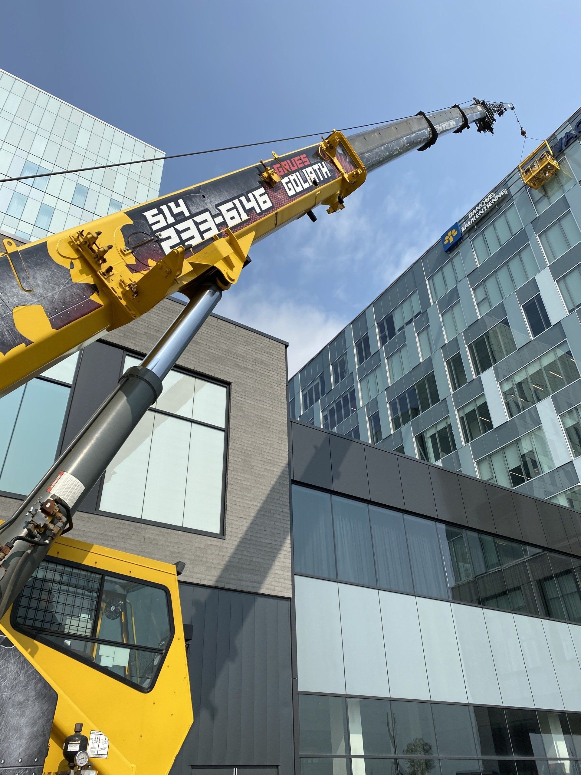 Grue jaune soulevant près de bâtiments modernes sous un ciel bleu.