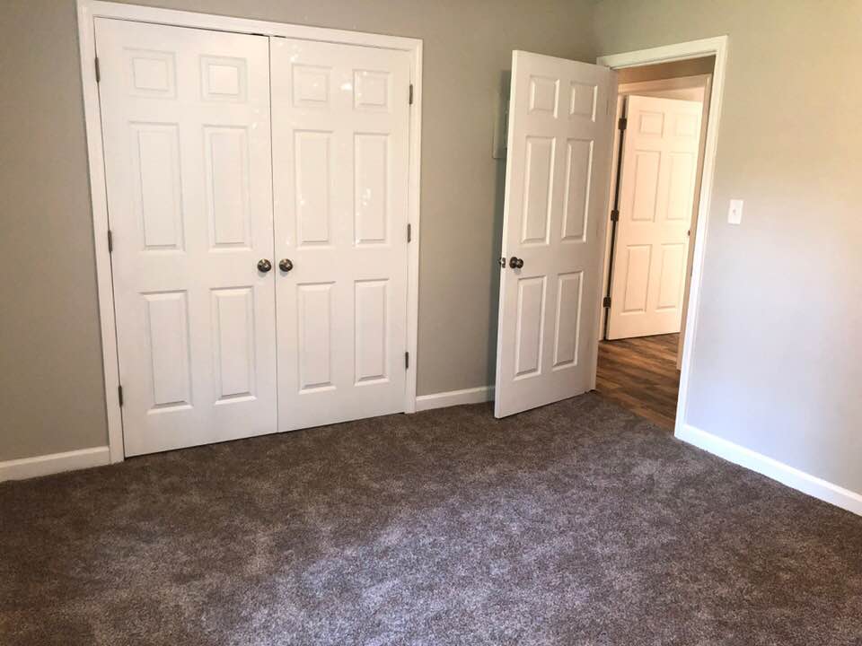 An empty bedroom with two closets and a carpeted floor.
