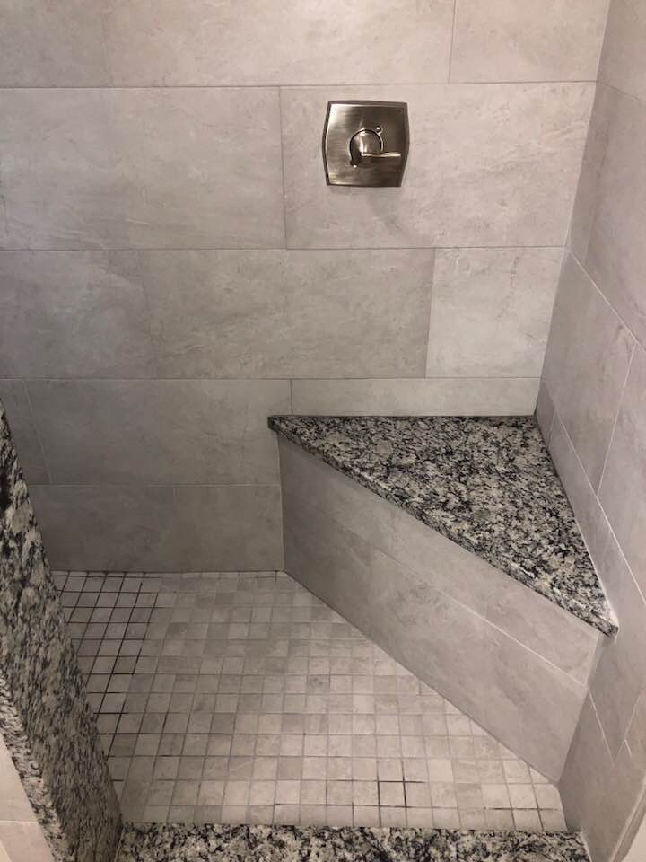 A shower with a granite bench and a shower head.