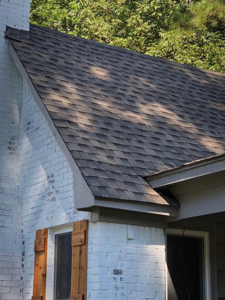 A white brick house with a brown roof and wooden shutters