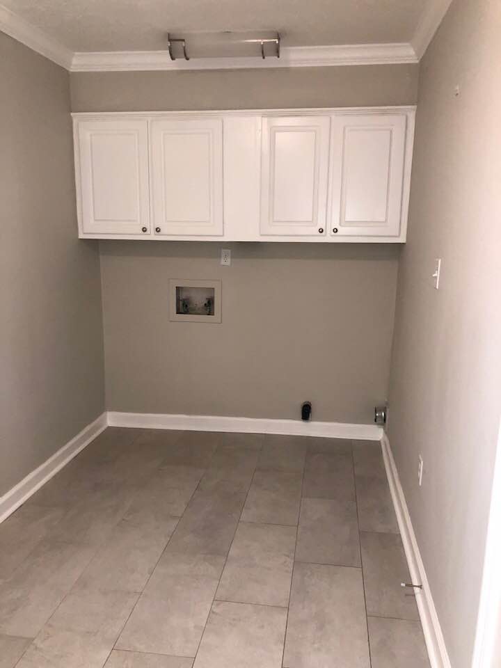 An empty laundry room with white cabinets and tile floors.