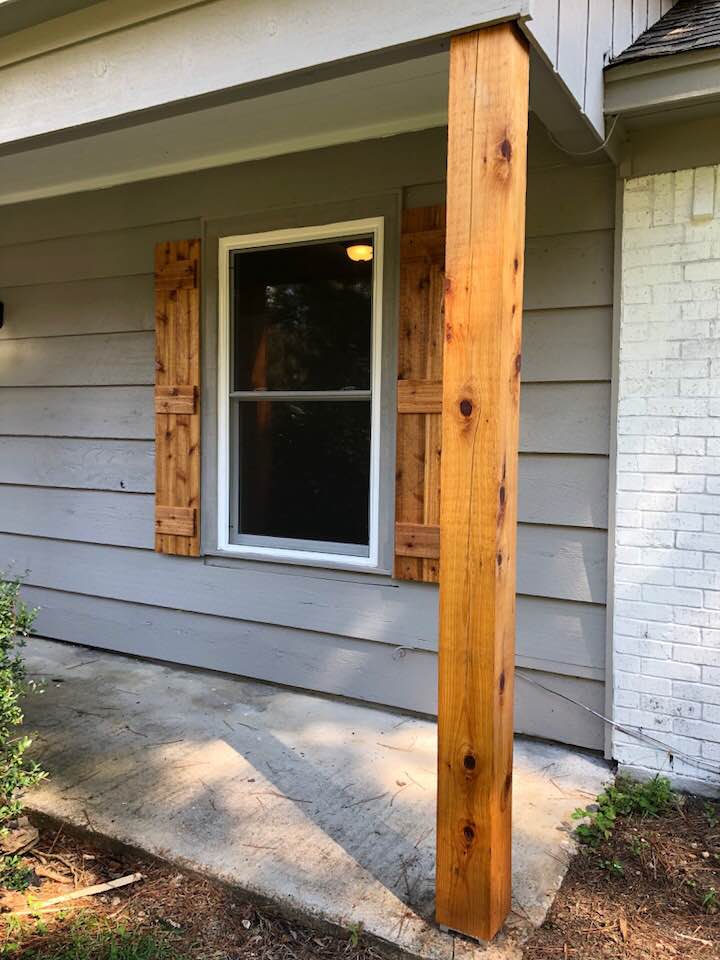A wooden post is sitting on the side of a house next to a window.