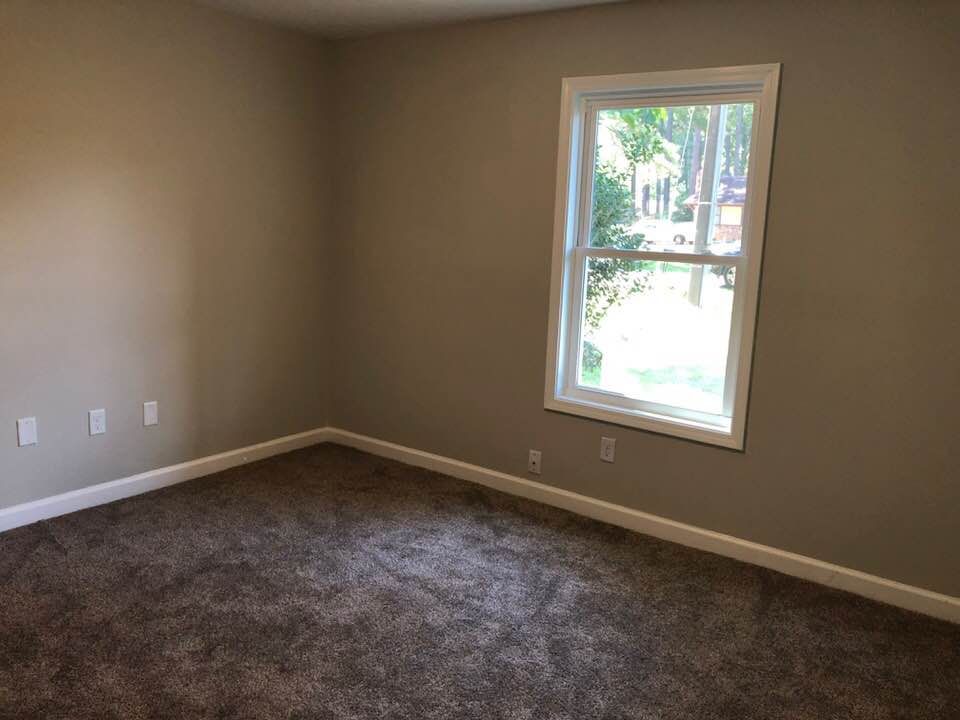 An empty bedroom with a window and a brown carpet.