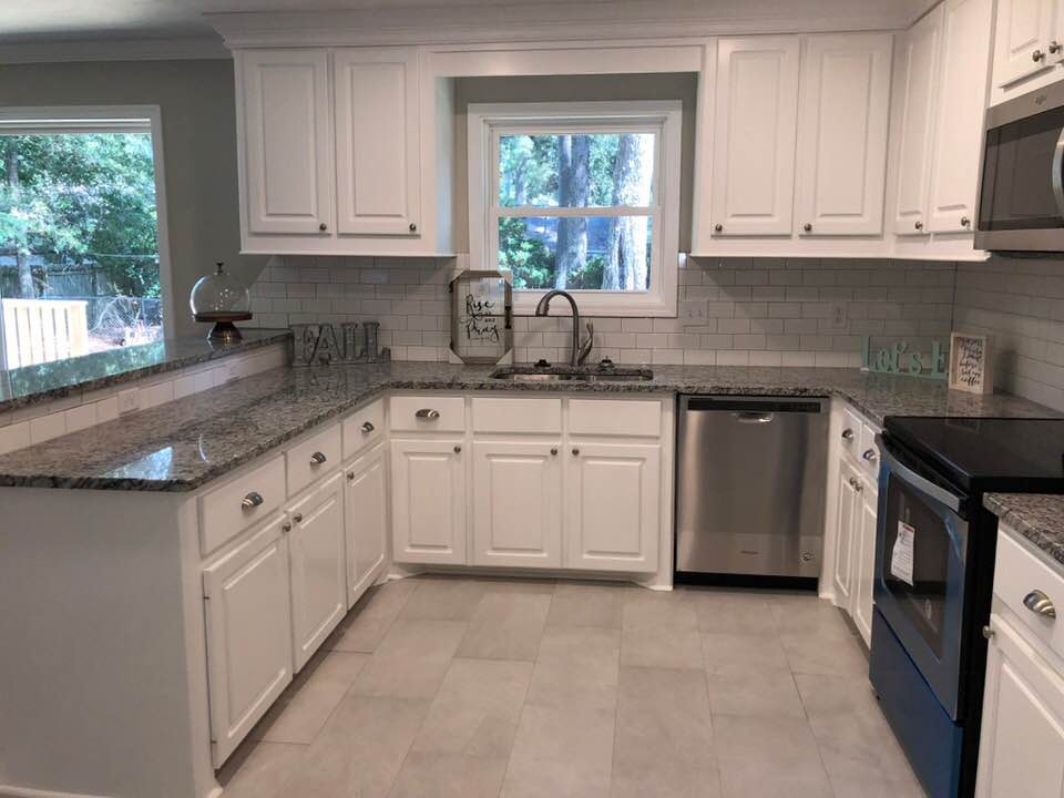 A kitchen with white cabinets , granite counter tops , stainless steel appliances and a window.