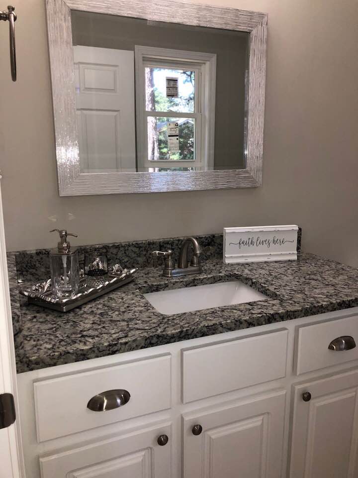 A bathroom with a sink , mirror and granite counter top.